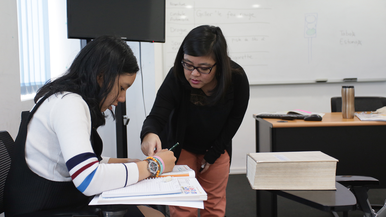 Guru perempuan menunjuk materi di buku pelajar yang sedak duduk