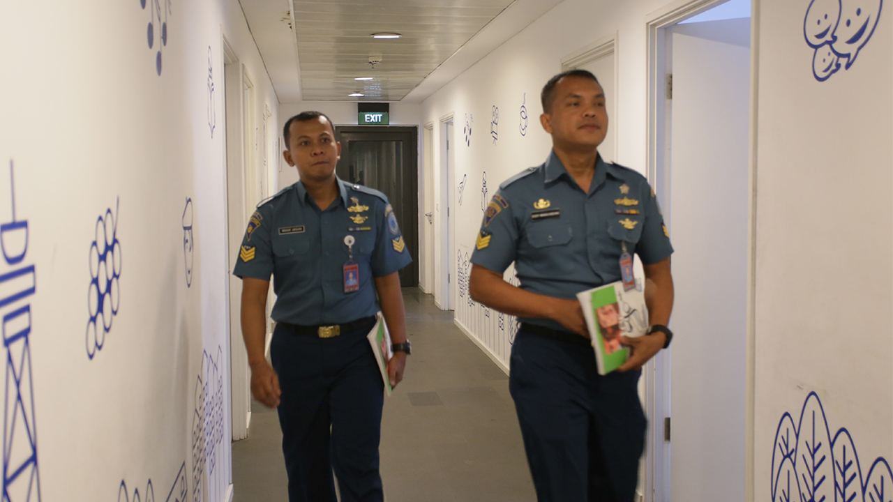 Dua laki-laki berseragam berjalan di lorong sambil memegang buku.