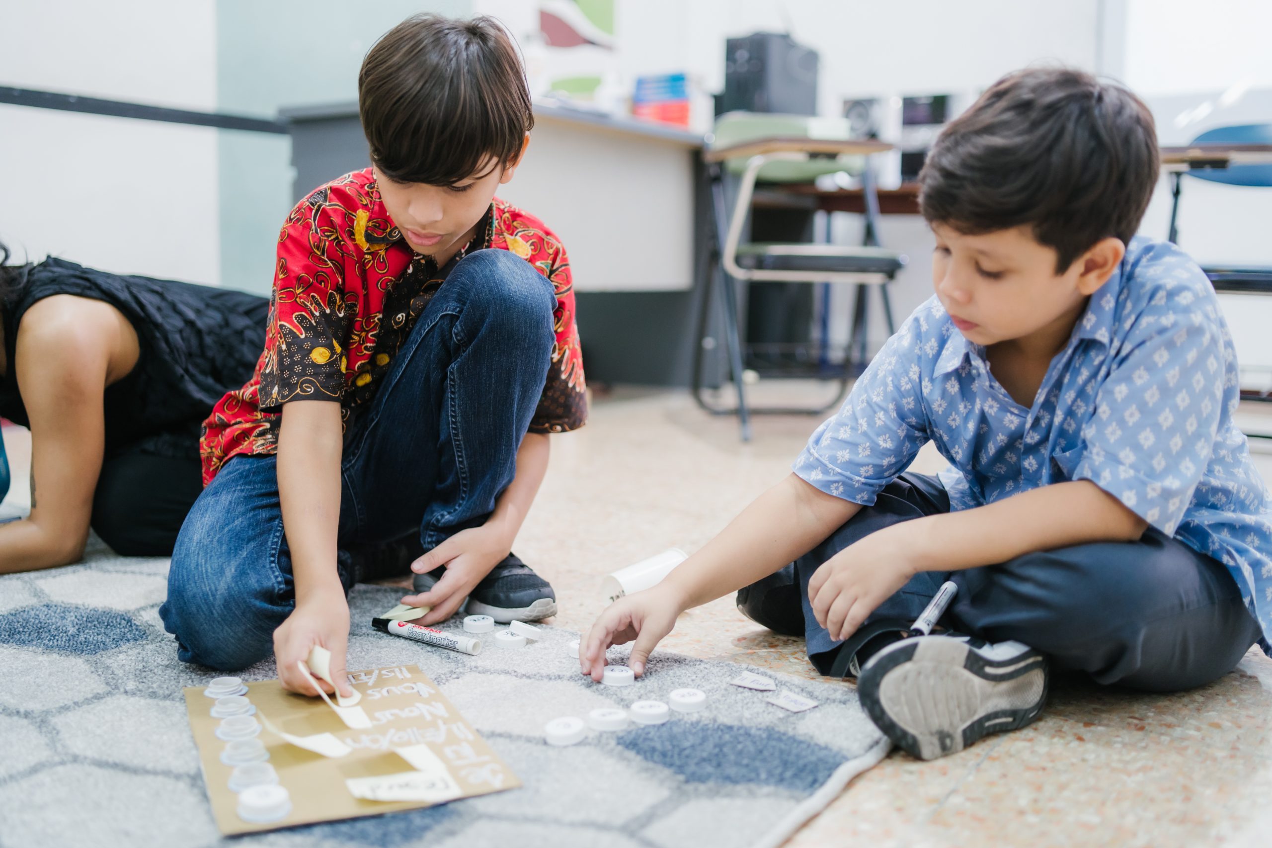 Dua anak pelajar bahasa Prancis sedang duduk di lantai dan menggerakan permainan